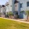 Row of modern townhomes with light blue facades, private front patios, and a landscaped walkway surrounded by greenery under a bright sun