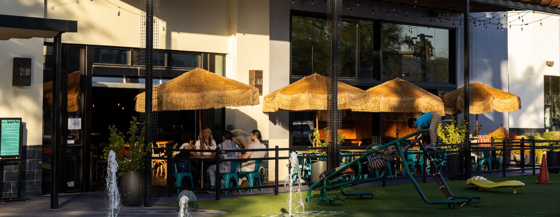 Outdoor dining area with a cozy firepit, surrounded by friends enjoying food and drinks under warm ambient lighting.